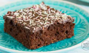 Ein Stück saftiger Schokokuchen vom Blech, mit Schokoladenglasur und bunten Streuseln, auf einem türkisfarbenen Teller.