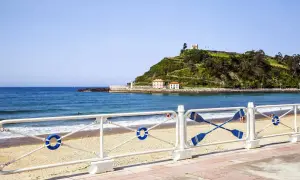 La **playa de Santa Marina** con su arena dorada, el mar azul y una colina verde coronada por un edificio blanco.