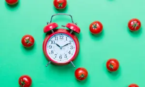 Czerwony budzik i pomidorki na zielonym tle. Czy to symbol techniki "pomodoro" do efektywnej pracy?