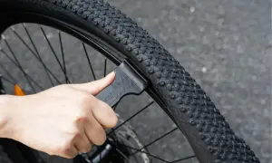 Dłoń używa czarnej łyżki do opon rowerowych, aby zdjąć oponę z obręczy. To pokazuje, jakie łyżki do opon rowerowych są potrzebne do naprawy.