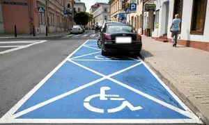 Niebieskie pole z białym symbolem wózka inwalidzkiego to **miejsce dla niepełnosprawnych**. Zaparkowany czarny samochód zajmuje ten specjalny parking.