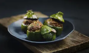 Trois courgettes rondes farcies, garnies d'une préparation savoureuse, reposent sur une assiette sombre, posée sur un plateau en bois vieilli.