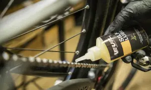 Rękawiczka z czarną buteleczką oleju do łańcucha rowerowego. Aplikator precyzyjnie nanosi smar, by łańcuch działał płynnie.
