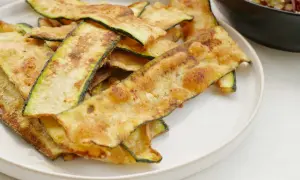 Krispiga, gyllene skivor av friterad zucchini ligger staplade på en vit tallrik, redo att avnjutas som ett lätt tilltugg.