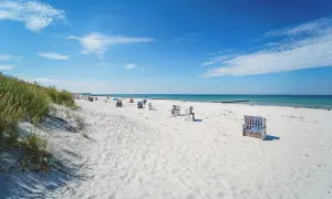 Ein sonniger Hiddensee Strand mit vielen Strandkörben, feinem Sand und dem blauen Meer.