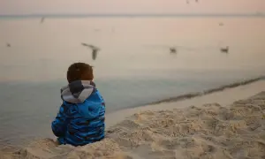 Chłopiec w niebieskiej bluzie siedzi na plaży, obserwując mewy. Spokojna atmosfera nad morzem może pomóc w tym, jak wyciszyć dziecko nadpobudliwe.