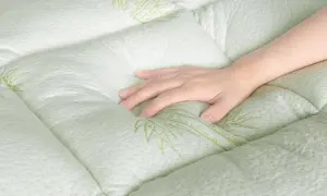 A hand rests on a quilted, light green mattress with a subtle bamboo leaf pattern. Experience the comfort and breathability of bamboo sleeping mat benefits.