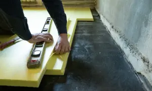 Ręce układają żółty styropian pod wylewkę, używając poziomicy. Unikaj błędów przy układaniu styropianu pod wylewkę.