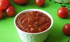 Domowy sos do pizzy, gęsty i aromatyczny, otoczony świeżymi pomidorami na zielonym tle. Idealny do każdej pizzy!