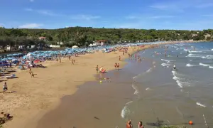 Una giornata di sole sulla **spiaggia di Bescile**, con ombrelloni colorati, bagnanti che giocano e si rilassano, e il mare che invita a un tuffo.