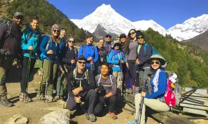 Grupa turystów z plecakami i kijkami trekkingowymi pozuje na tle ośnieżonych gór podczas Manaslu Circuit Trek.