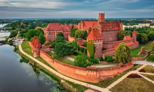 Malbork, najwiekszy zamek w Polsce, majestatycznie wznosi się nad rzeką Nogat, otoczony ceglanymi murami i zielenią.