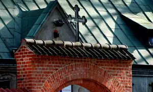 Ceglany łuk i dach kościoła z krzyżem. Nawet apostata mógłby tu znaleźć spokój, patrząc na te dachówki.