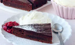 En bit fransk chokladtårta med vispad grädde och hallonsylt. Pudrad med florsocker.