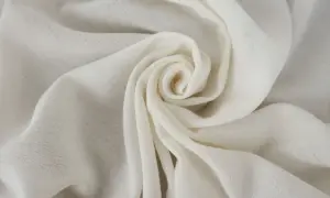 Delikatna, kremowa tkanina w groszki, ułożona w kształt spirali, przypomina płatki róży.
