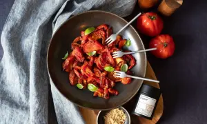 Schüssel mit karamellisierten Tomaten, garniert mit Basilikum. Daneben frische Tomaten, Ingwer-Gewürz und ein kleiner Napf mit Ingwerpulver.