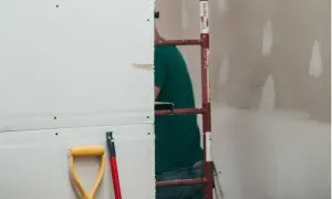 Prace remontowe w toku. Zastanawiasz się, ile schnie gips szybkoschnący? Na pierwszym planie łopata i trzonek, w tle pracownik budowlany.