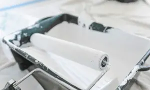 Un rouleau à peinture blanc est posé dans un bac en plastique noir, prêt à enlever la peinture.