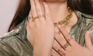 Manos adornadas con varios anillos dorados y un collar grueso, mostrando cómo llevar anillos de manera elegante.
