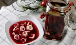 Talerz z uszkami w czerwonym barszczu obok słoika z zakwasem z buraków. W tle świąteczne dekoracje.