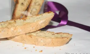 Två mandelkakor, perfekta för ditt biscotti recept, ligger på en vit duk. En lila sidenband ligger bakom.