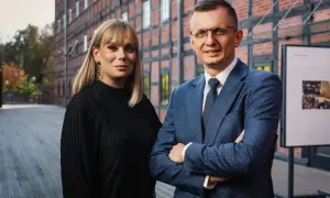 Para adwokatów, kobieta w czarnej bluzce i mężczyzna w niebieskiej marynarce, stoją przed ceglanym budynkiem.