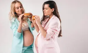 Dwie ciężarne kobiety w pastelowych marynarkach trzymają burgery, ulegając ciążowemu głodowi.