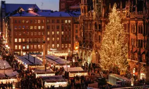 Beleuchteter Weihnachtsbaum und geschäftiger Weihnachtsmarkt bis Silvester, mit Buden und Menschen vor historischen Gebäuden.