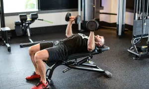 Mężczyzna wykonuje ćwiczenie dumbbell press na ławce w siłowni, podnosząc ciężarki nad klatką piersiową.