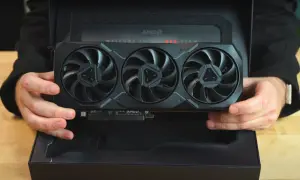 Ręce trzymają kartę graficzną Radeon RX 7900 XTX z trzema wentylatorami, wyjętą z czarnego pudełka z napisem "WELCOME TO RED TEAM".