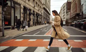 Kobieta w beżowym płaszczu i żółtych sneakersach przechodzi przez pasy. Idealne buty do trencza na miejski spacer.