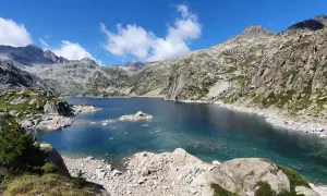 Lago azul cristalino en el corazón del Vall de Boí Aigüestortes, rodeado de imponentes montañas rocosas y vegetación escasa.