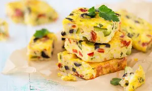Carrés de frittata colorés, une recette avec des oeufs, garnie de légumes et d'olives, sur du papier sulfurisé.