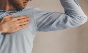 Hombre con camisa azul mostrando manchas de sudor bajo el brazo. Una solución para quitar manchas de sudor es necesaria.