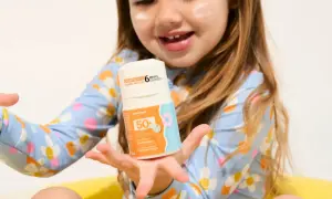 Un enfant tient un flacon de crème solaire UVA UVB 50+. La crème est conçue pour les enfants dès 6 mois.