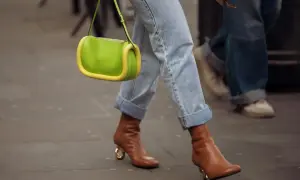 Brązowe buty na obcasie z złotym detalem, jeansy z podwiniętymi nogawkami i jaskrawozielona torebka tworzą modne stylizacje damskie.