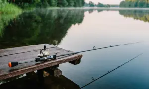 Wędka leży na drewnianym pomoście nad spokojnym jeziorem Tuchlin. Wczesny poranek, mgła unosi się nad wodą.