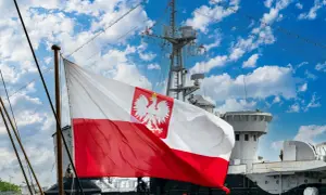 Flaga bandery z orłem dumnie powiewa na tle błękitnego nieba z chmurami, nad pokładem statku.