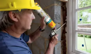 Obrero con casco amarillo aplica espuma expansiva para sellar ventanas exterior.