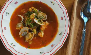 En skål med bouillabaisse med musslor och räkor, perfekt att servera med ett glas vin.