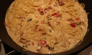 Krämig baconpasta i en stekpanna, med spaghetti och bitar av knaperstekt bacon.