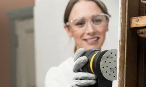 Mujer con gafas de seguridad usa lijadora orbital para restaurar madera, una forma eficiente de como lijar madera sin lija.