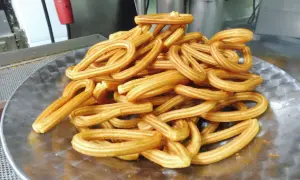 Montón de churros dorados en forma de lazo sobre un plato metálico.