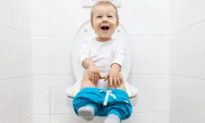 Bambino felice sul water, pantaloni abbassati, pronto per la sua prima cacca nel water.
