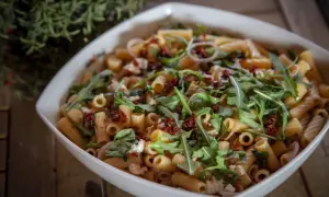 Ein köstlicher nudelsalat mit getrockneten tomaten, Rucola und Mozzarella in einer weißen Schüssel.
