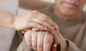Dłoń opiekunki na dłoni starszego mężczyzny, który trzyma laskę. Wsparcie i troska, jak przy leczeniu np. chorobą Parkinsona, gdzie **Madopar** może pomóc.