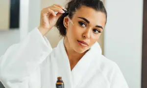 Une femme applique un sérum sur son visage, peut-être un mélange d'acide azélaïque et de vitamine C, pour une peau éclatante.