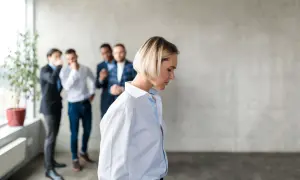 Kobieta odwraca się od grupy mężczyzn, którzy szepczą i wskazują na nią. To obraz niewłaściwego zachowania przełożonego wobec pracownika.