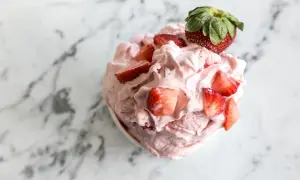 Un délice rose et crémeux : un sorbet fraise garni de morceaux de fruits frais et d'une fraise entière sur un fond marbré.