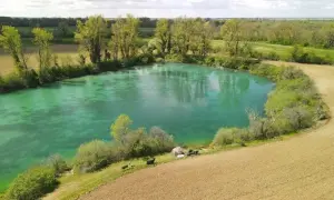 Idyllischer Paylake in Frankreich mit türkisfarbenem Wasser, umgeben von grüner Vegetation und Feldern. Angler haben ihr Lager aufgeschlagen.